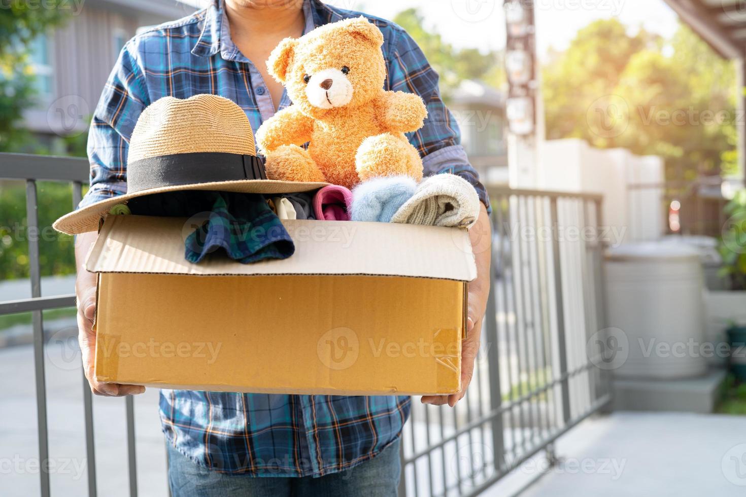 Holding clothing donation box with used clothes and doll at home to support help for poor people in the world. photo