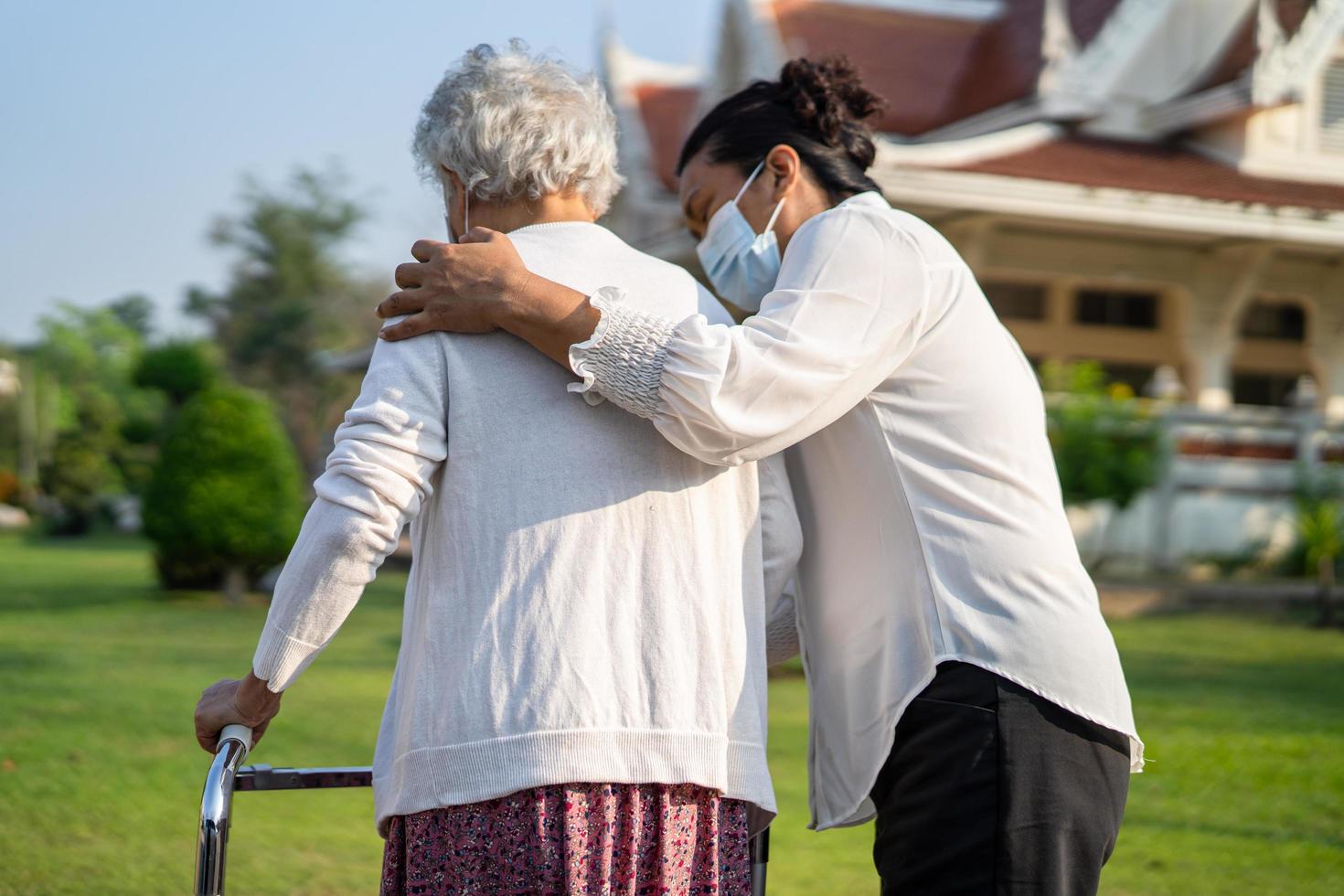 cuidador ayuda y cuida a una anciana asiática o anciana que usa andador con buena salud mientras camina en el parque en felices vacaciones frescas. foto