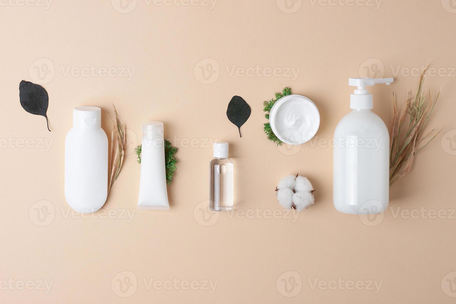 Cosmetic composition with cosmetic skin care products and flowers on pastel beige background. Flat lay, copy space photo