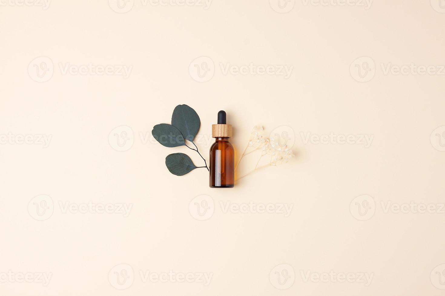 Cosmetic bottle with flowers and eucalyptus on pastel beige background. Flat lay, copy space photo