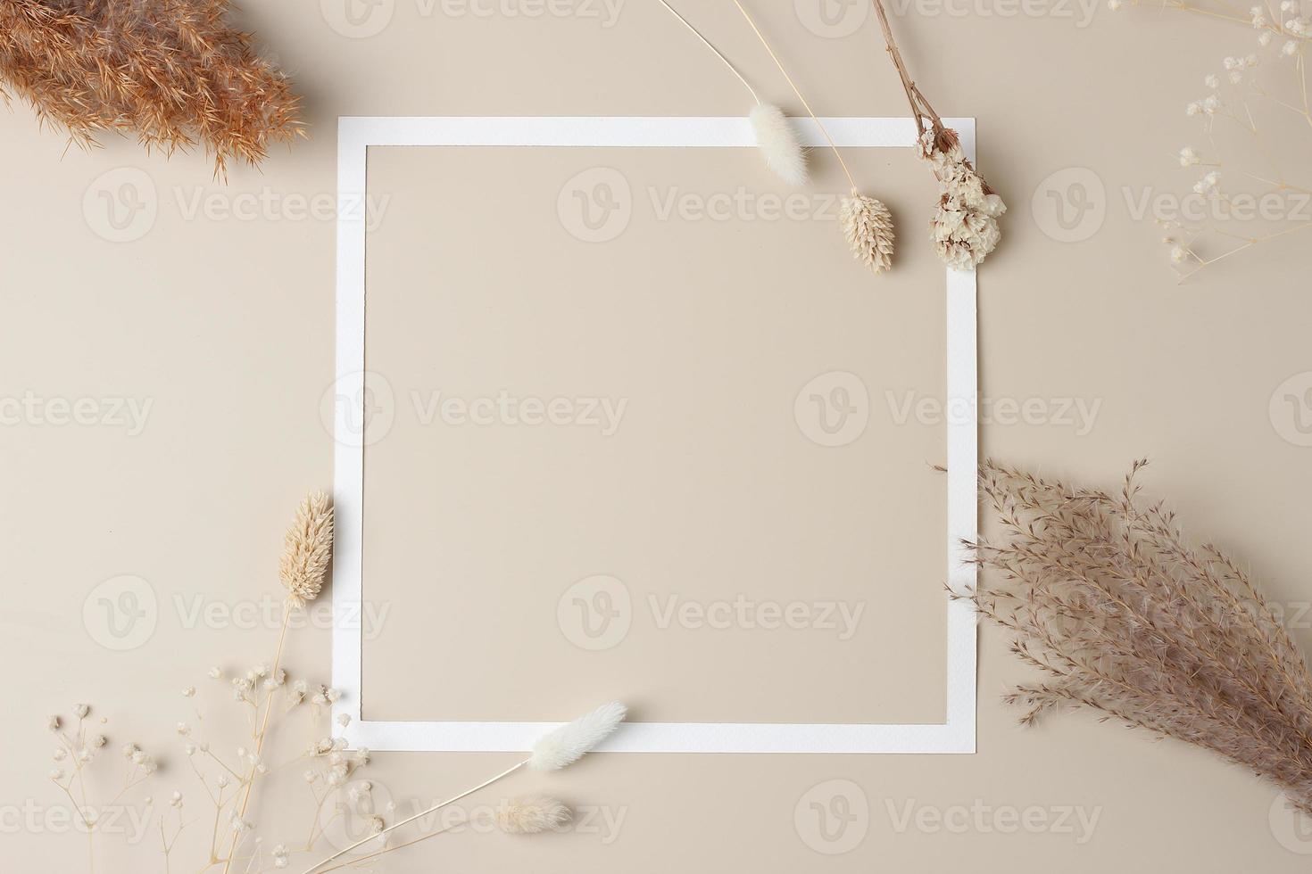 White frame with flovers on beige background. Flat lay, copy space. photo