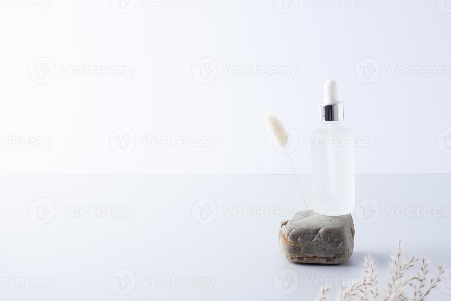 botella cosmética con flores y piedra sobre fondo gris. cerrar, copiar espacio foto