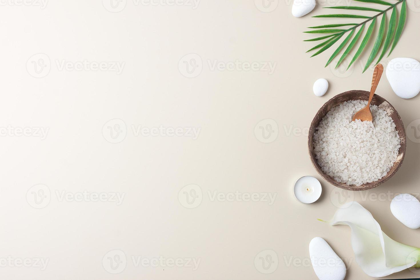 Spa background with bowl of salt, white stones, candles, palm leaf and white flower on pastel beige. Flat lay,copy space photo