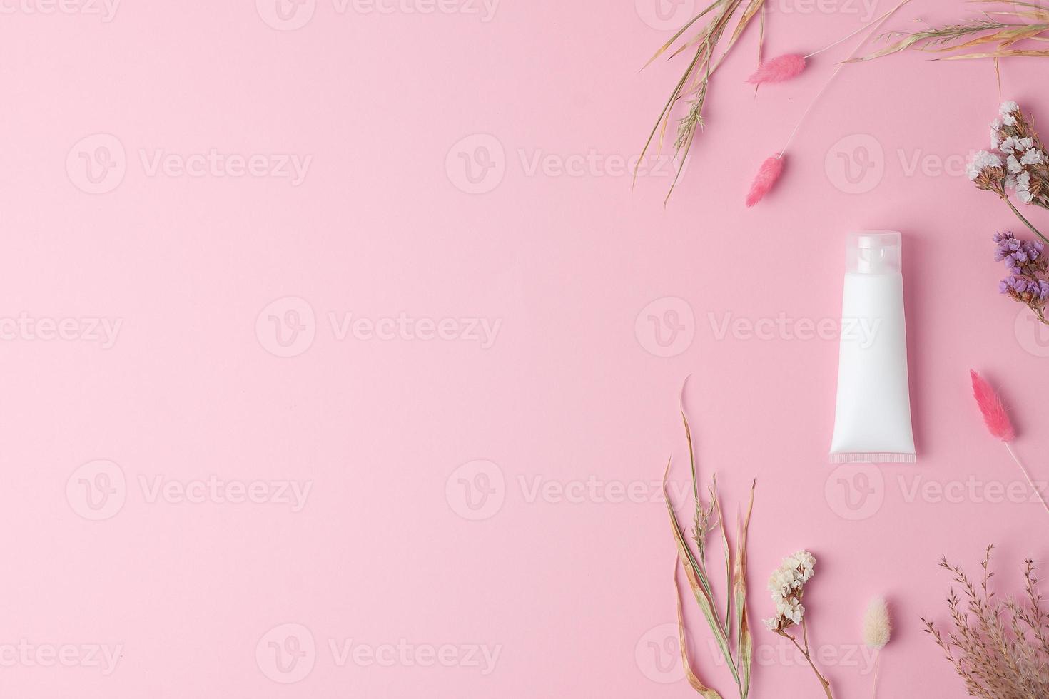 White tube of cosmetic cream with flowers on pink background. Flat lay, copy space photo