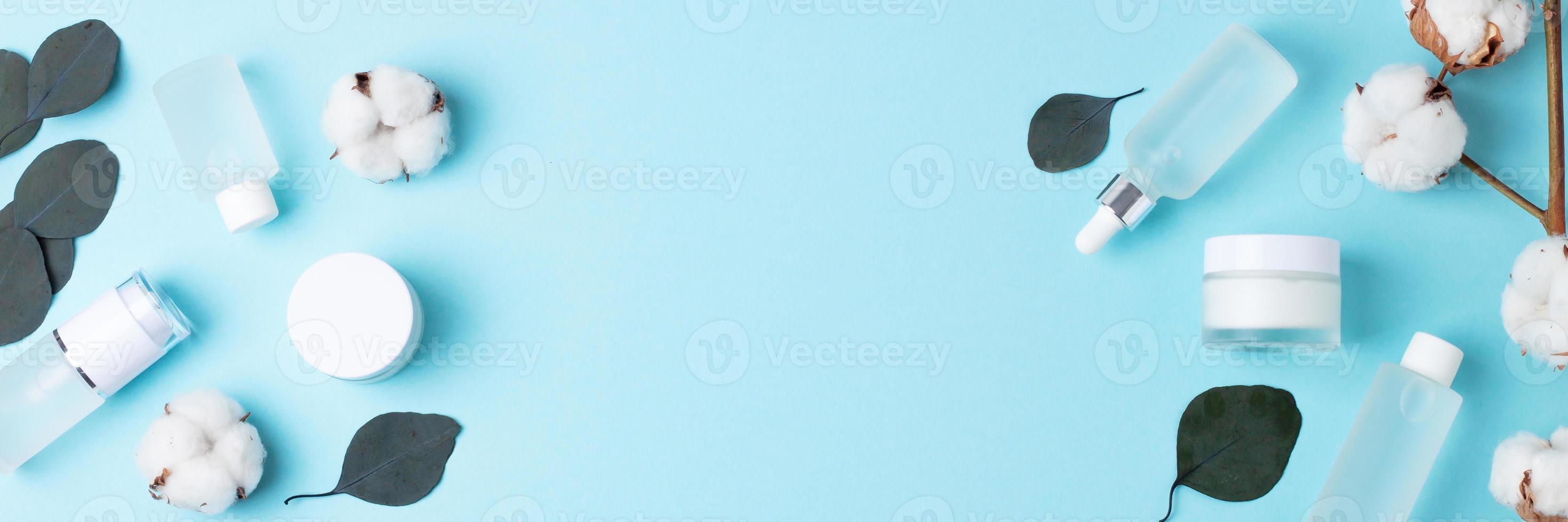 Cosmetic skin care products with flowers and eucalyptus on blue background. Flat lay, copy space photo
