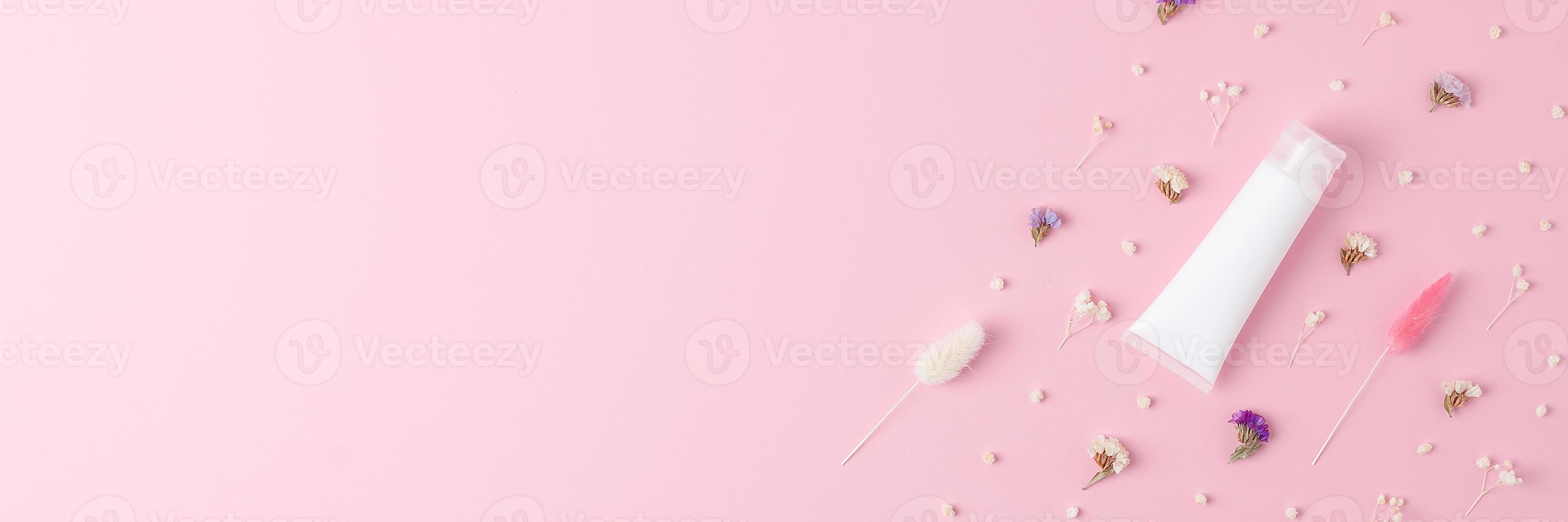 White tube of cosmetic cream with flowers on pink background. Flat lay, copy space photo