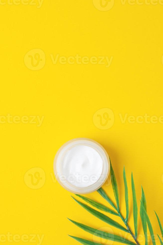 tarro de crema cosmética con rama de palma de hoja sobre fondo amarillo. endecha plana, espacio de copia foto