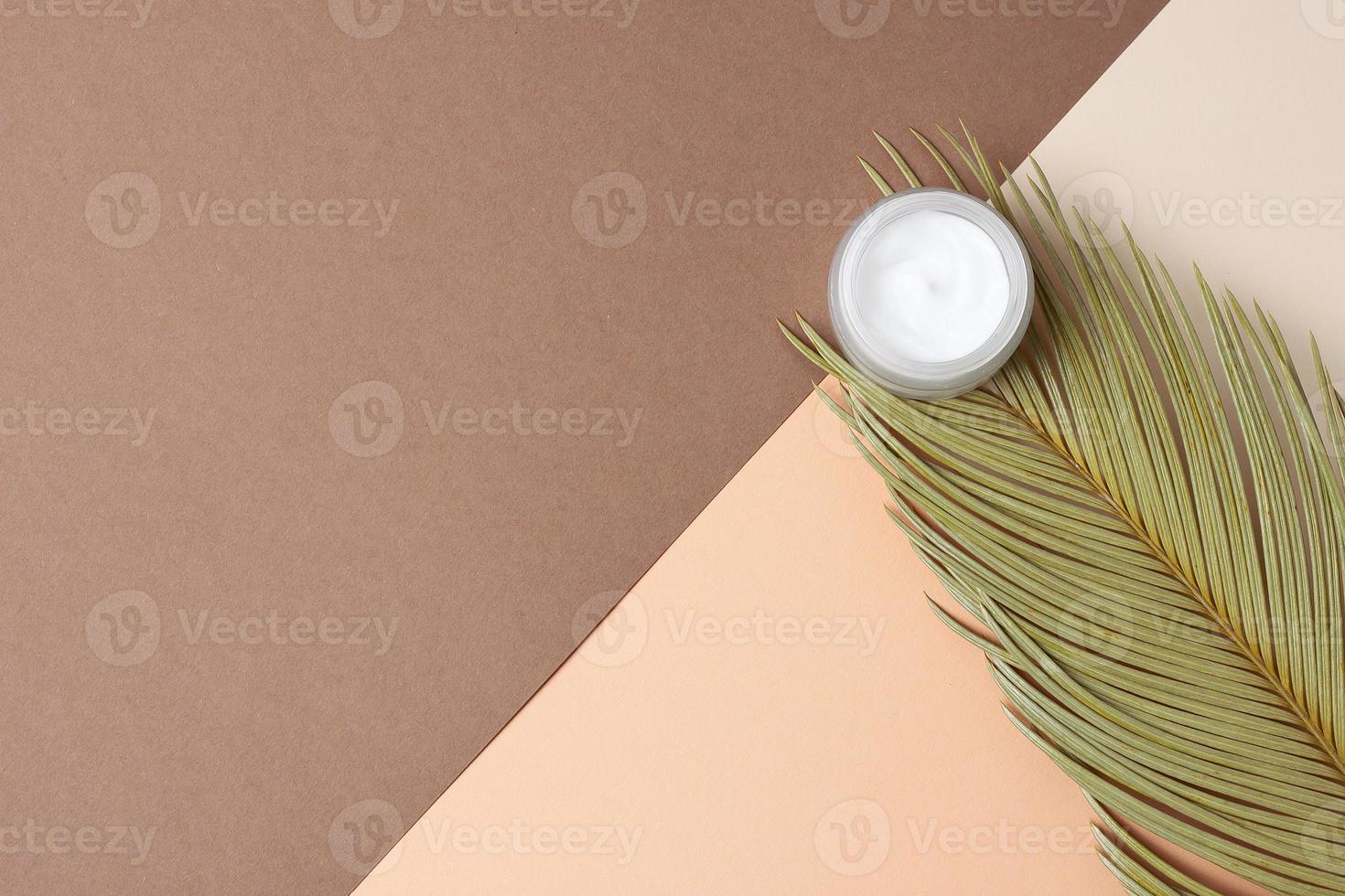 Jar of cosmetic cream with palm leaf on mixed color background. Flat lay, copy space photo