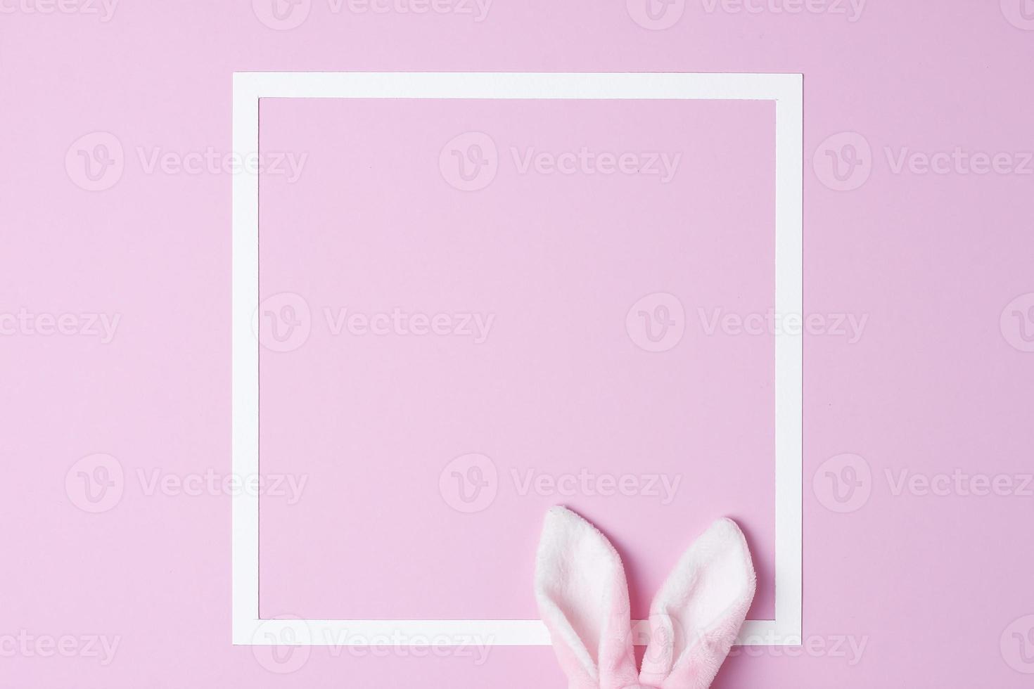 Bunny ears with white frame on pink background. Flat lay, copy space photo