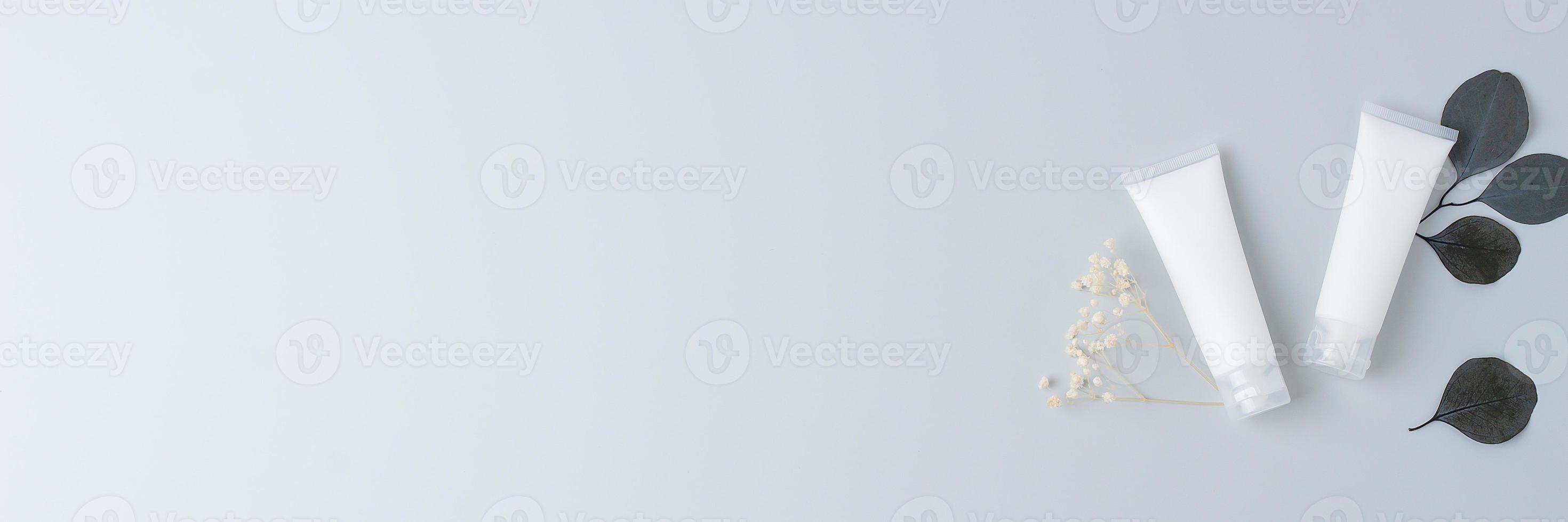 White tubes of cosmetic cream with eucalyptus natural background on grey background. Flat lay, copy space photo