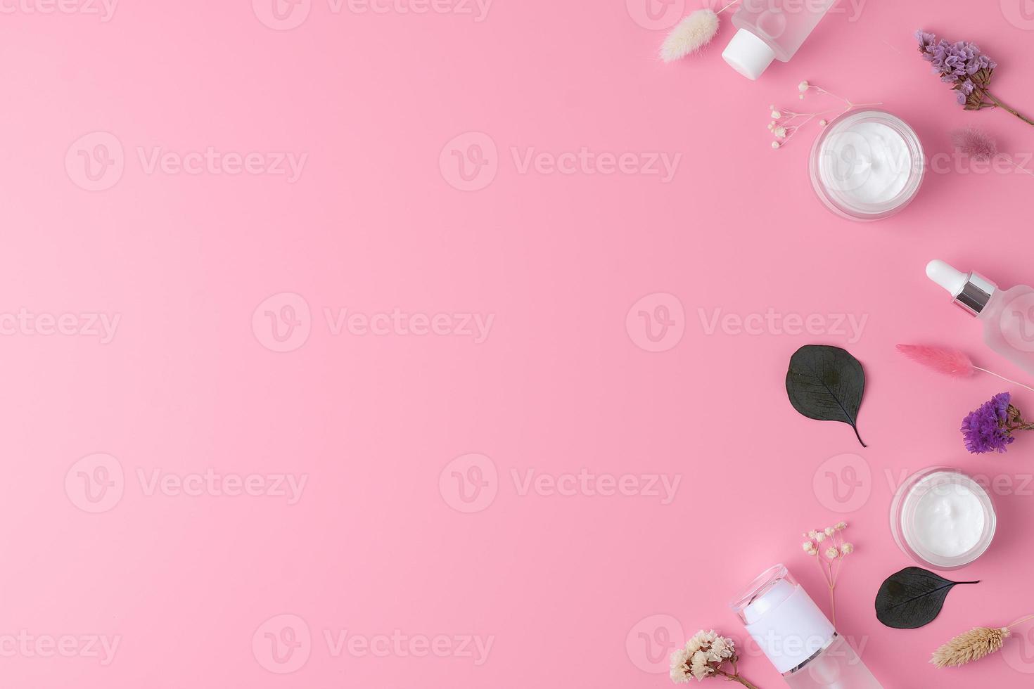 Skin care products on pink background with flowers, eucalyptus. Flat lay, copy space. photo