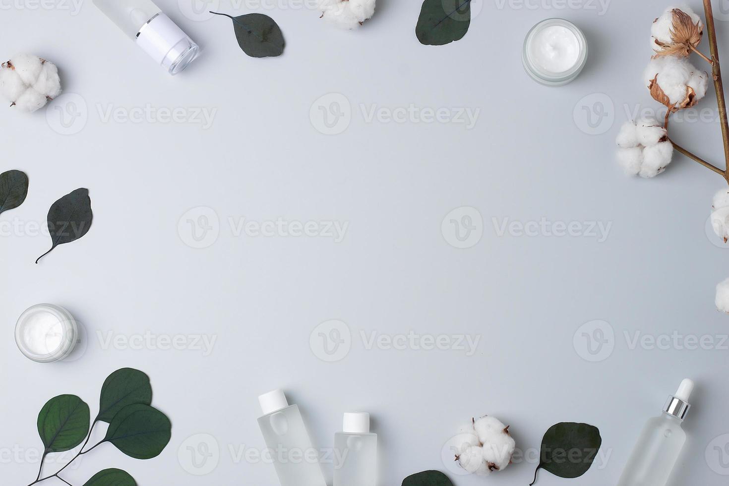 Cosmetic skin care products with flowers and eucalyptus on grey background. Flat lay, copy space photo