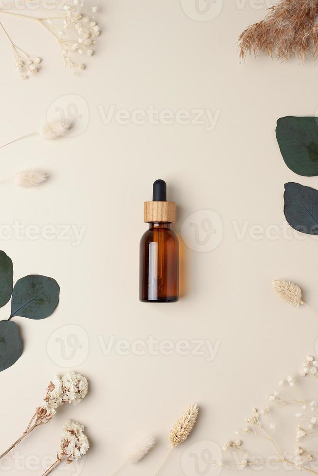botella cosmética con flores y eucalipto sobre fondo beige pastel. endecha plana foto