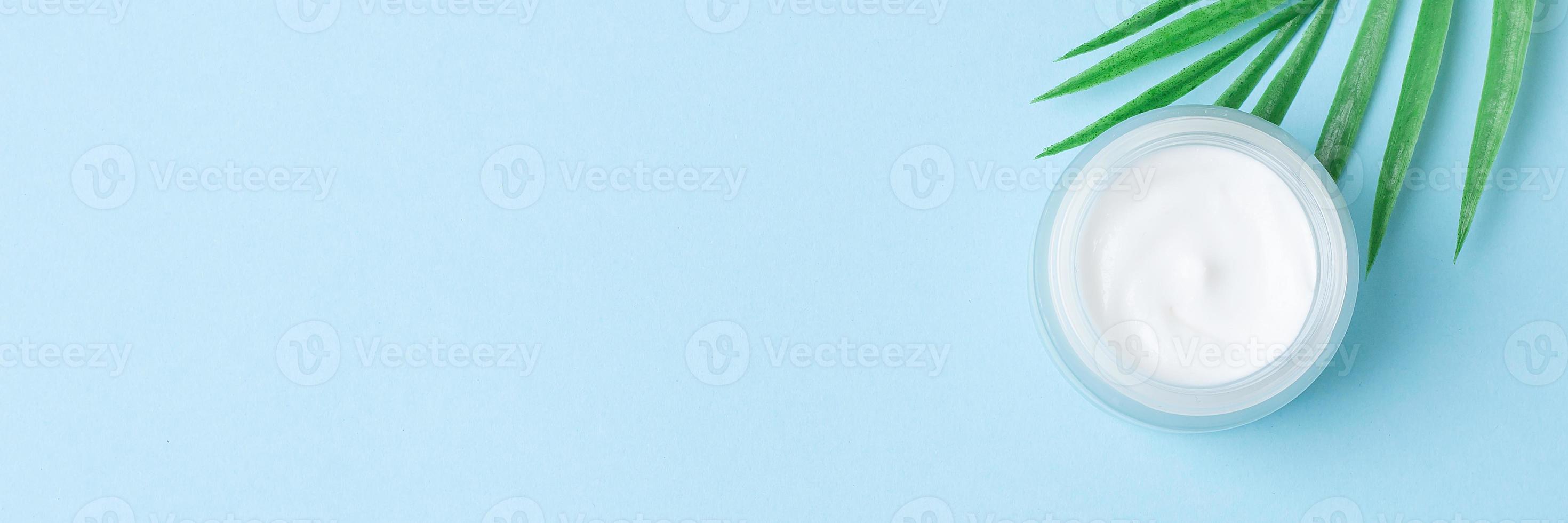 Jar of cosmetic cream with leaf palm branch on blue background. Flat lay, copy space photo