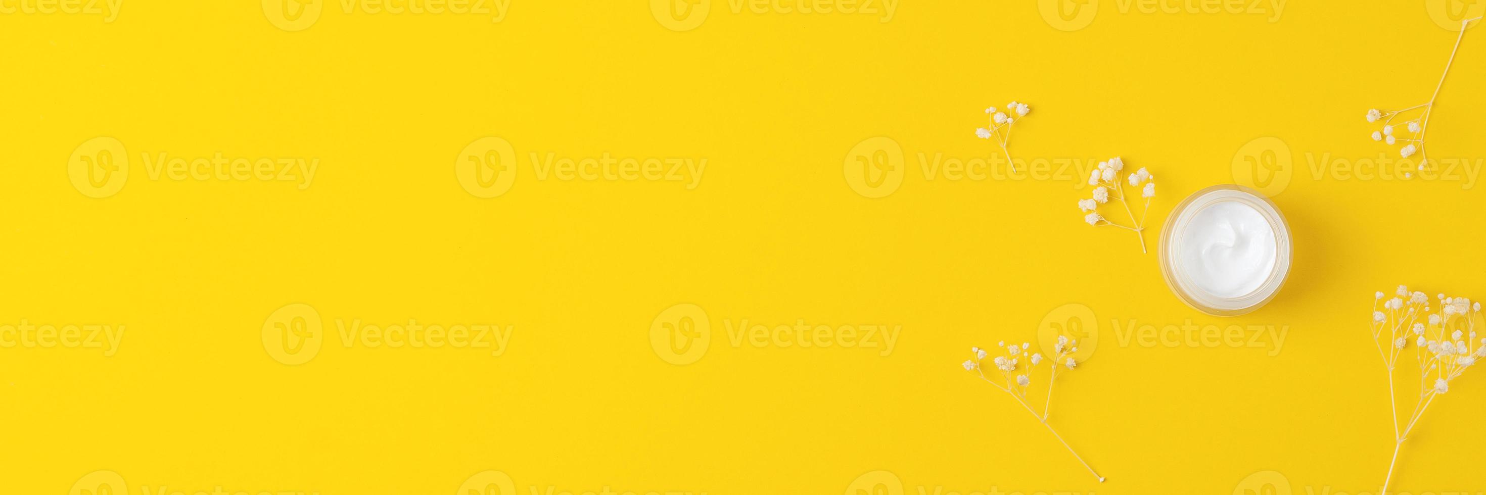 Jar of cosmetic cream with flowers on yellow background. Flat lay, copy space photo