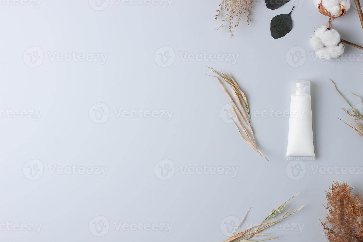 White tube of cosmetic cream with flowers on grey background. Flat lay, copy space photo