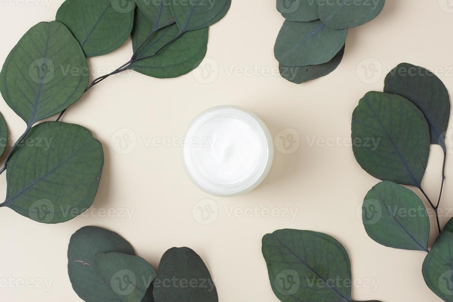 Jar of cosmetic cream with eucalyptus on pastel beige background. Flat lay, copy space photo