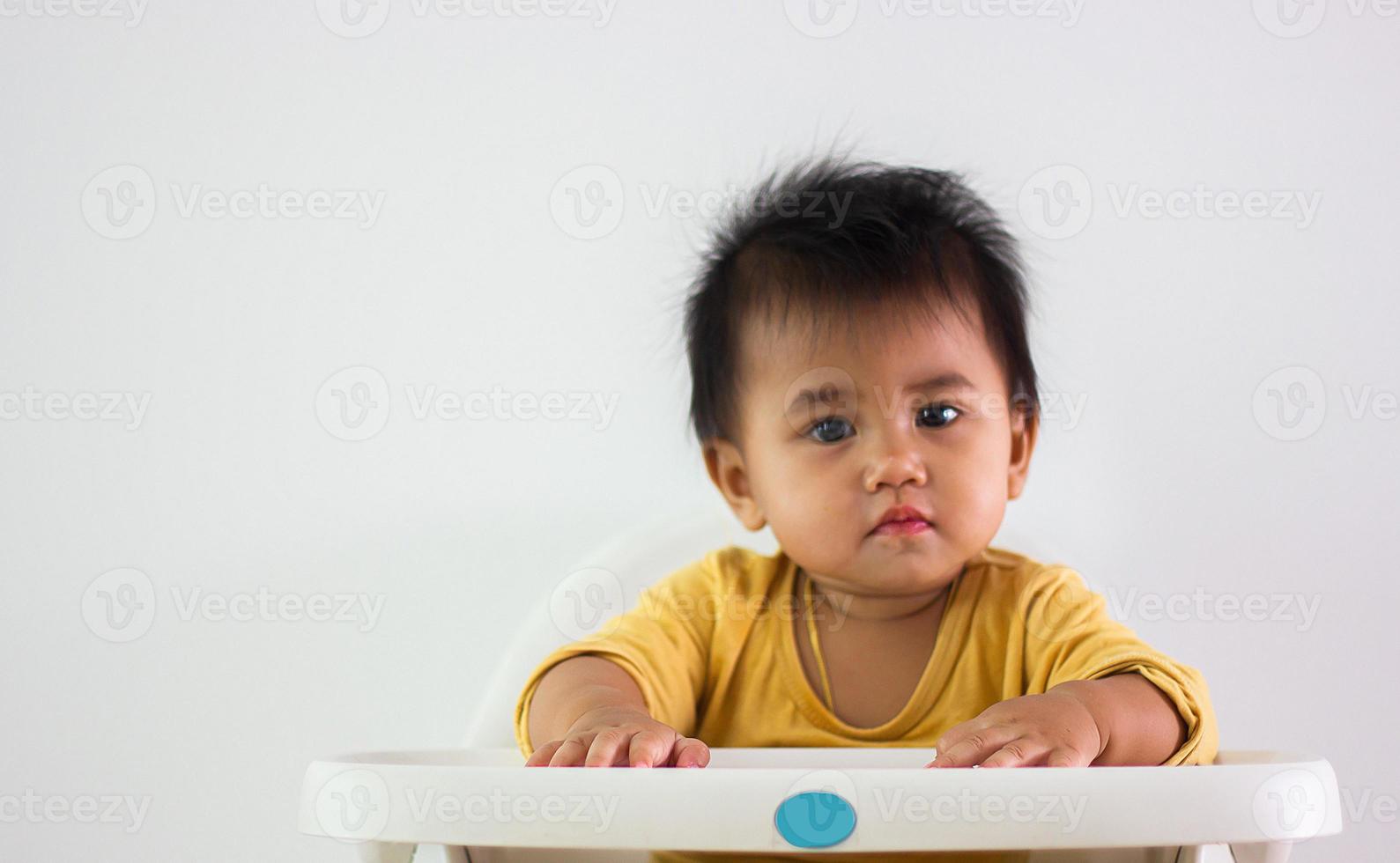 una niña de camisa amarilla de etnia asiática se sienta pacientemente en una silla sola en casa. expresión de la emoción, el entusiasmo, la infancia y la puerilidad. fuera esa linda guau cara felicidad vida foto