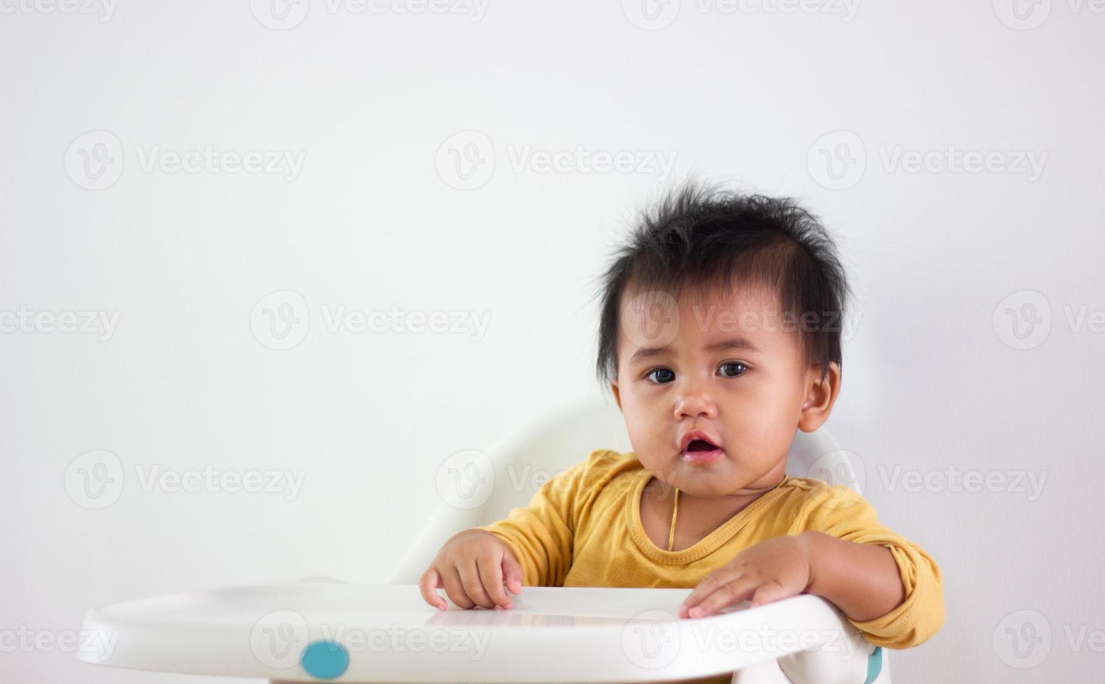 una niña de camisa amarilla de etnia asiática se sienta pacientemente en una silla sola en casa. expresión de la emoción, el entusiasmo, la infancia y la puerilidad. fuera esa linda guau cara felicidad vida foto