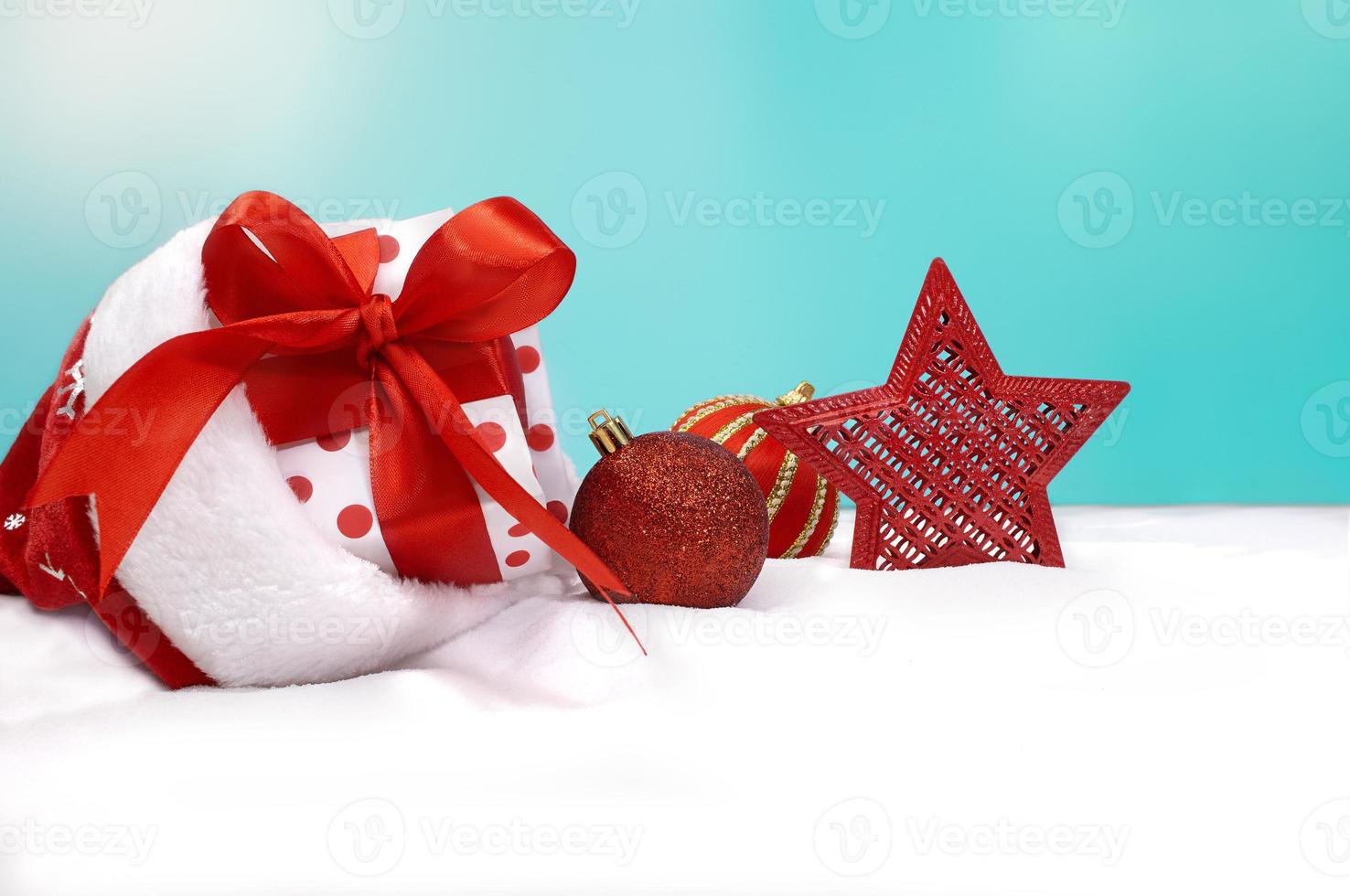 White gift box with dots in Santa' hat or sock, with red sparkling toys, star on snow, blue background in back. Christmas, New Year. Copy space photo