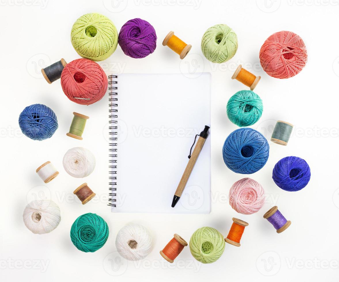 Multicolored balls and bobbins of woolen yarn, wooden thread sleeves on white isolated background. Notepad with pen. Needlework, handmade. view from above. Isolated. Copy space photo