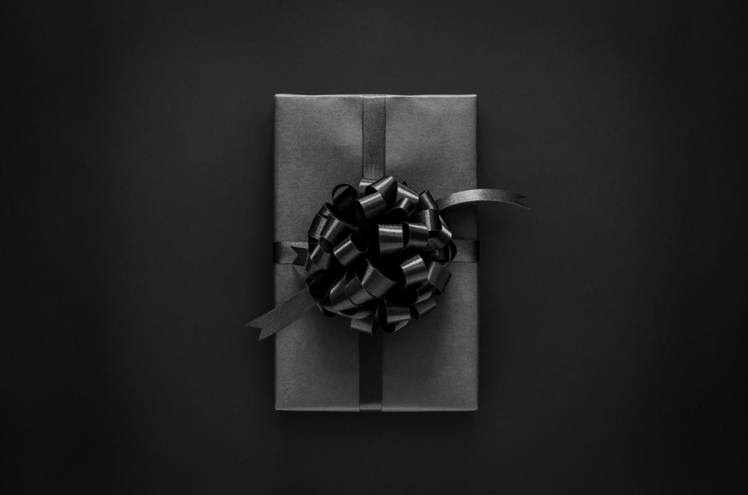 A black gift box with ribbon and price tag puts on black background. Black friday and Boxing day concept. photo