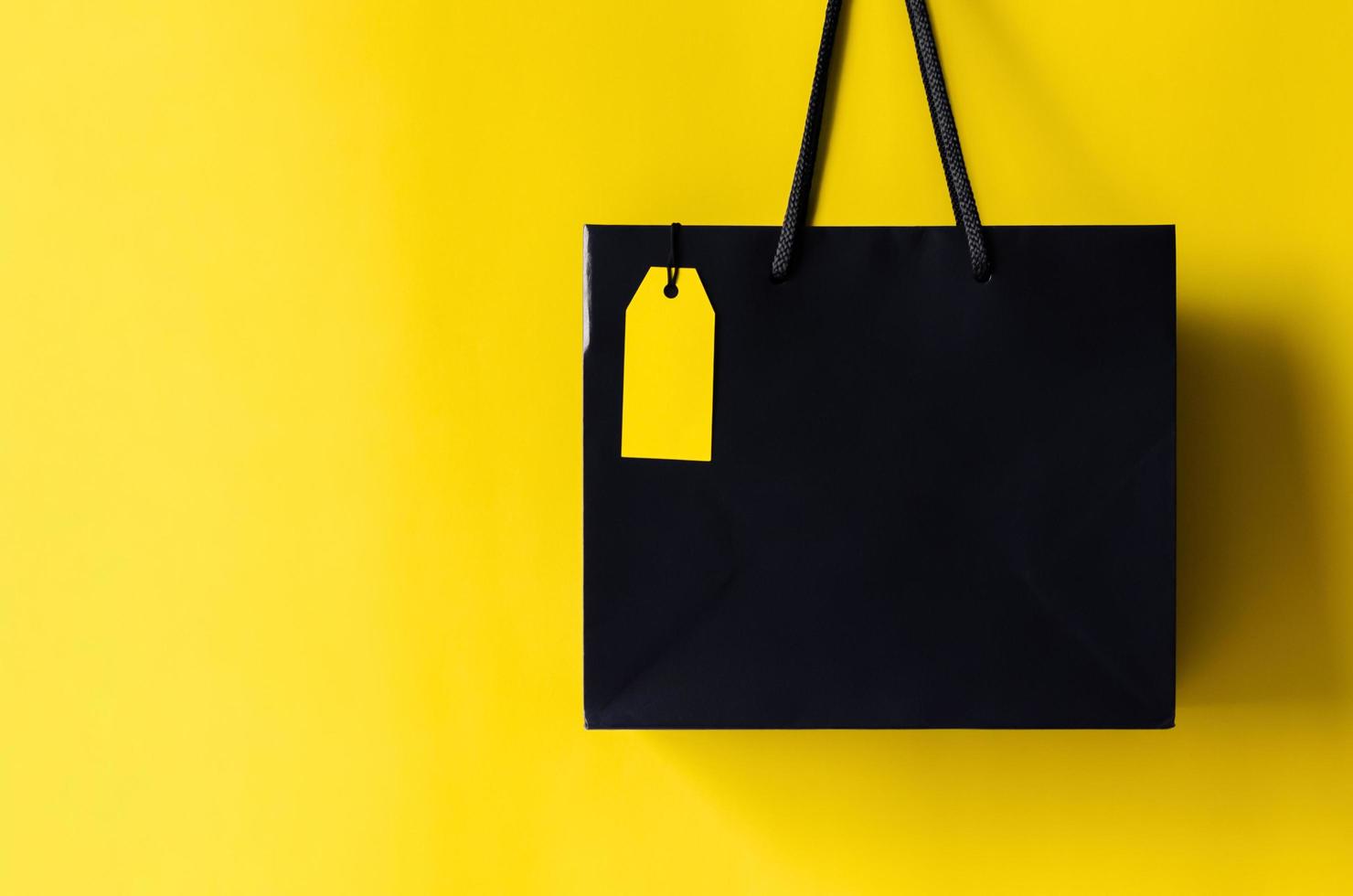 bolsa de compras negra con etiqueta de precio amarilla en blanco con fondo amarillo para el concepto de venta de compras de viernes negro. foto