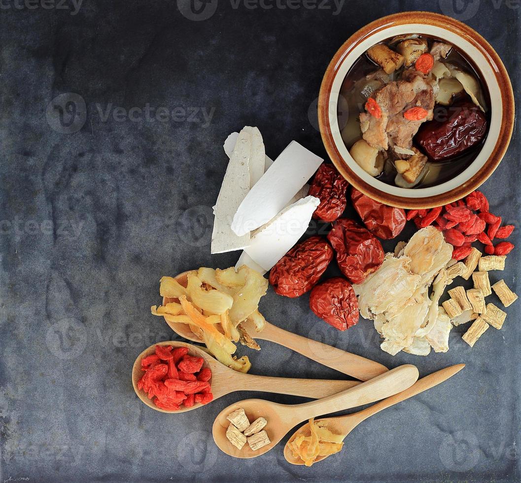 Top view of many chinese herbs with bowl of clear soup on black photo