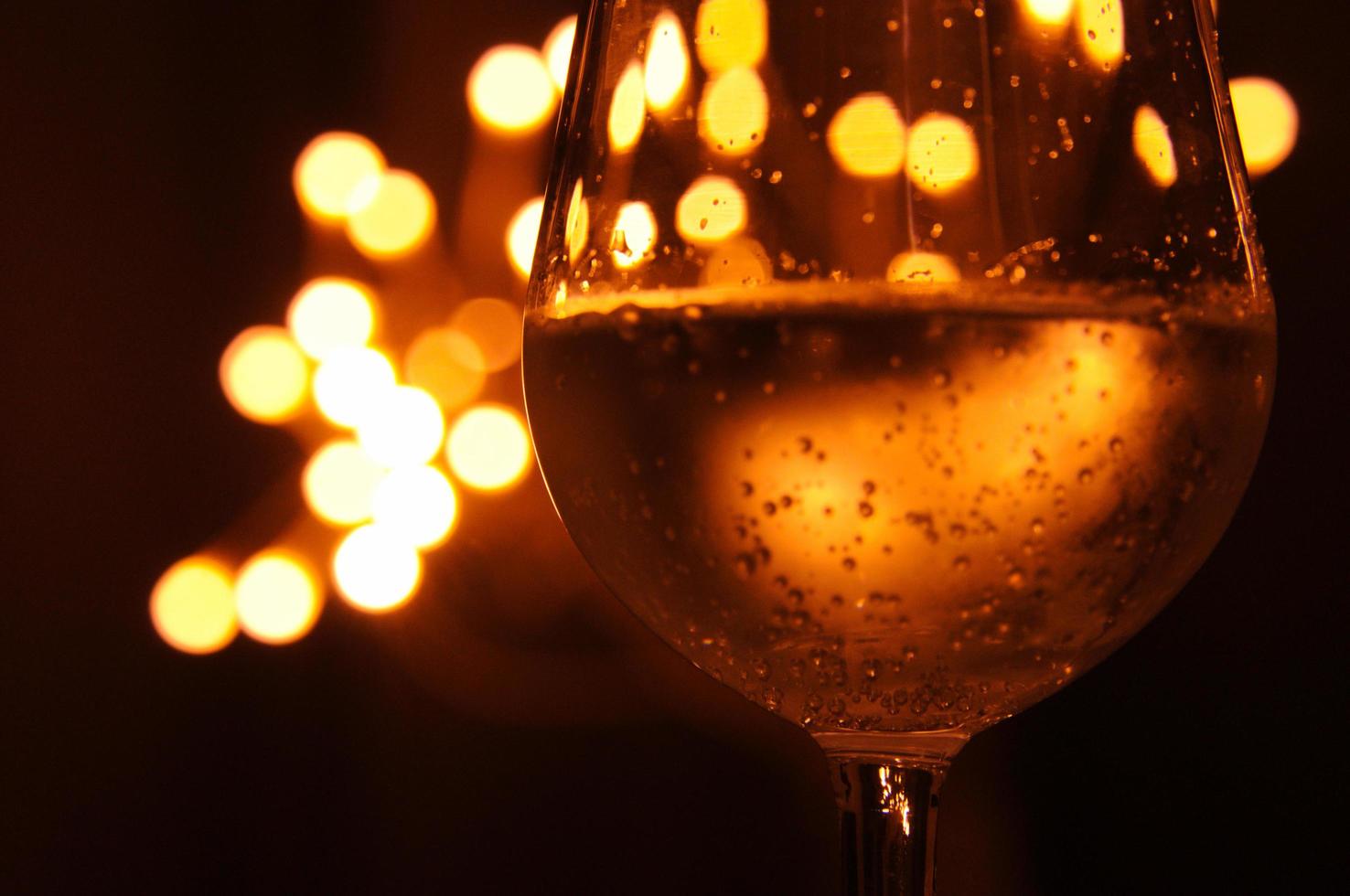 A glass of wine has the shadow of yellow and orange bokeh light on it which isolated on dark color background photo