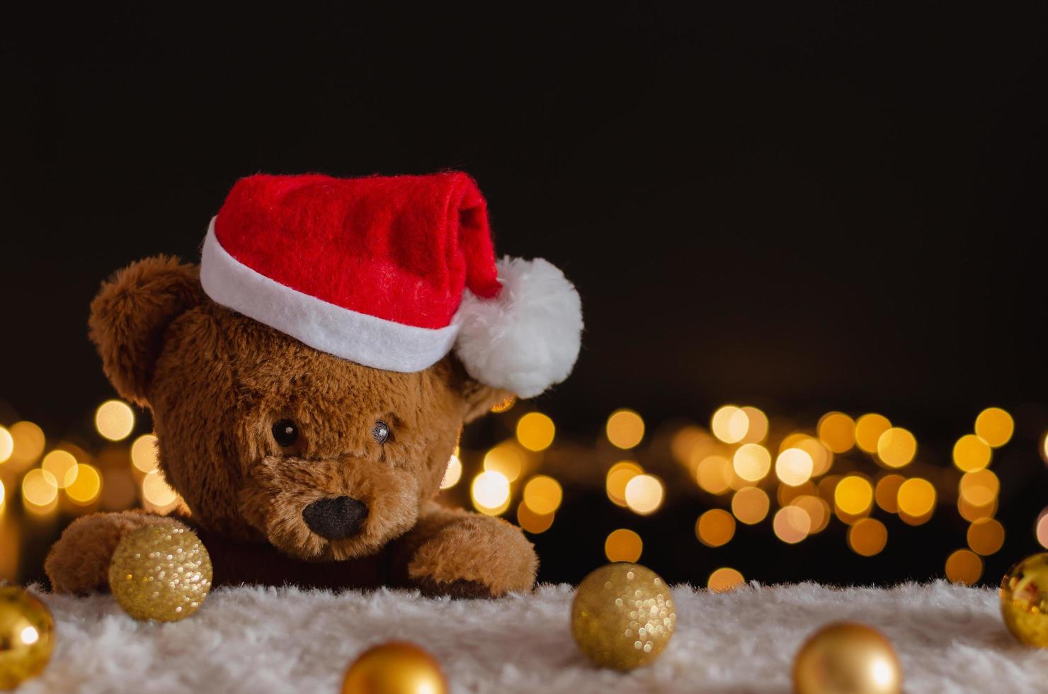 Brown teddy bear wearing santa claus hat with Christmas ornaments and lights background. photo