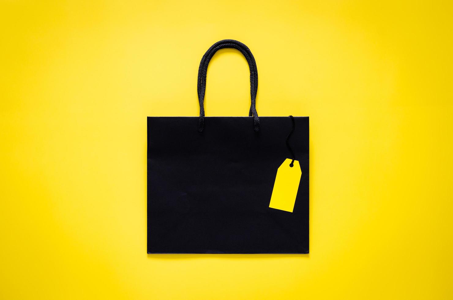 Black shopping paper bag with blank yellow price tag on yellow background for Black Friday shopping sale concept. photo
