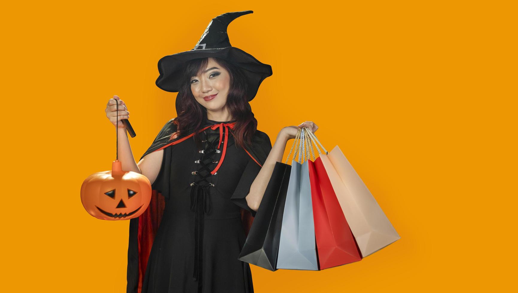 Asian girl in witch costume holding jack o lantern and shopping sale bag for halloween party trick or treat concept isolate on orange background photo
