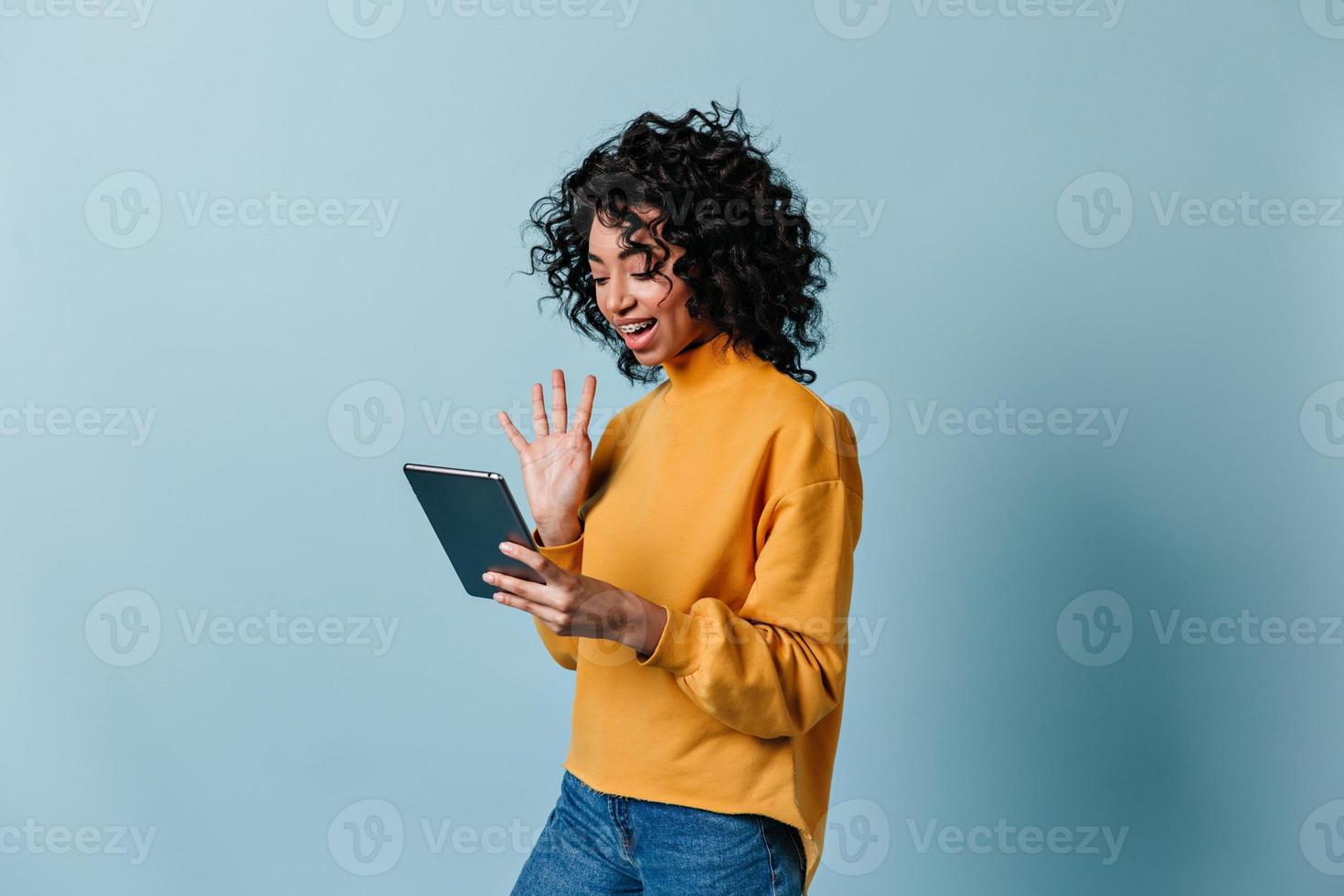 niña sonriente saludando con la mano en la pantalla de la tableta digital. encantadora mujer rizada usando video chat. foto