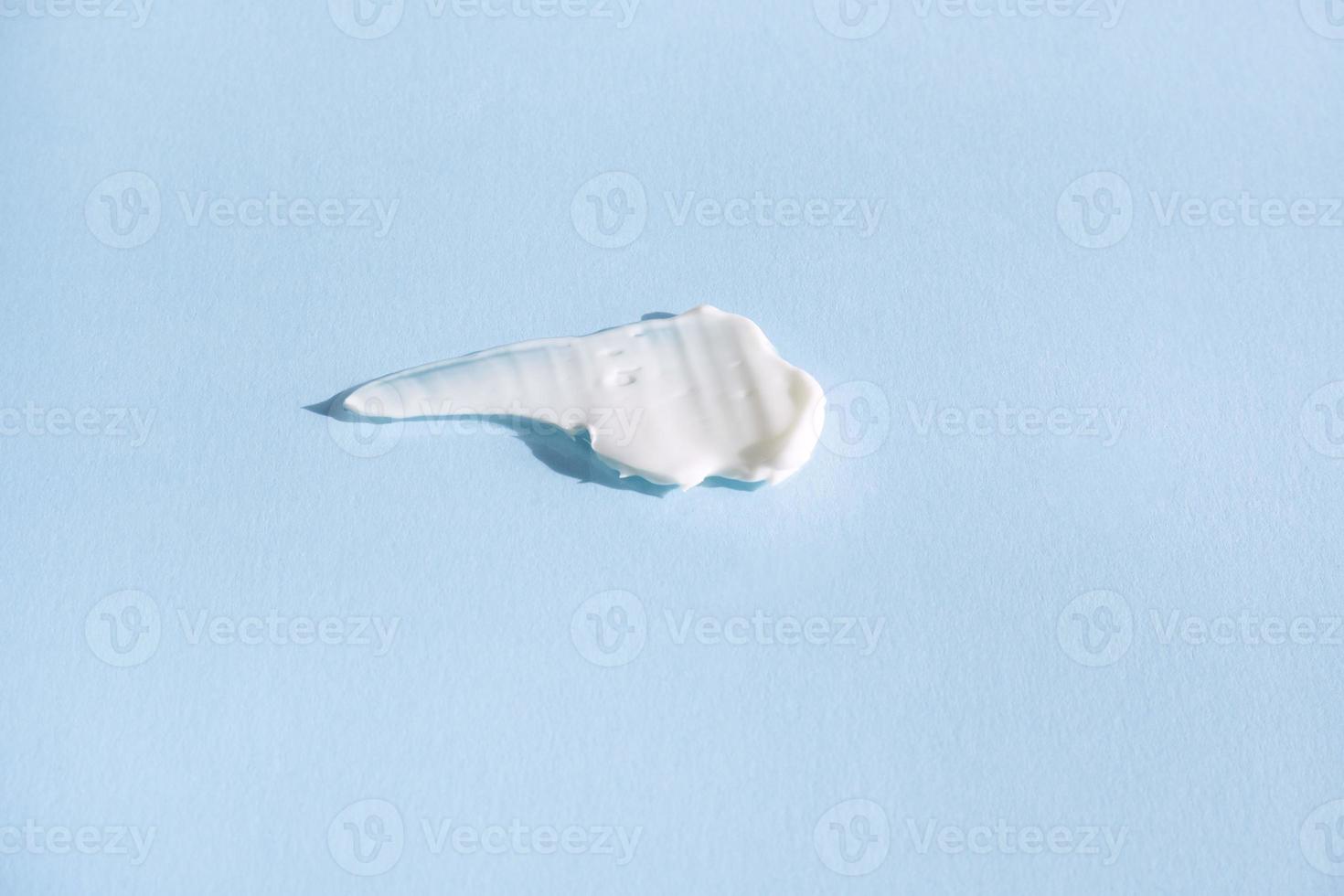 White smear of cosmetic cream on a blue background. Creamy base texture isolated. A smear of face cream. Close-up of creamy texture photo