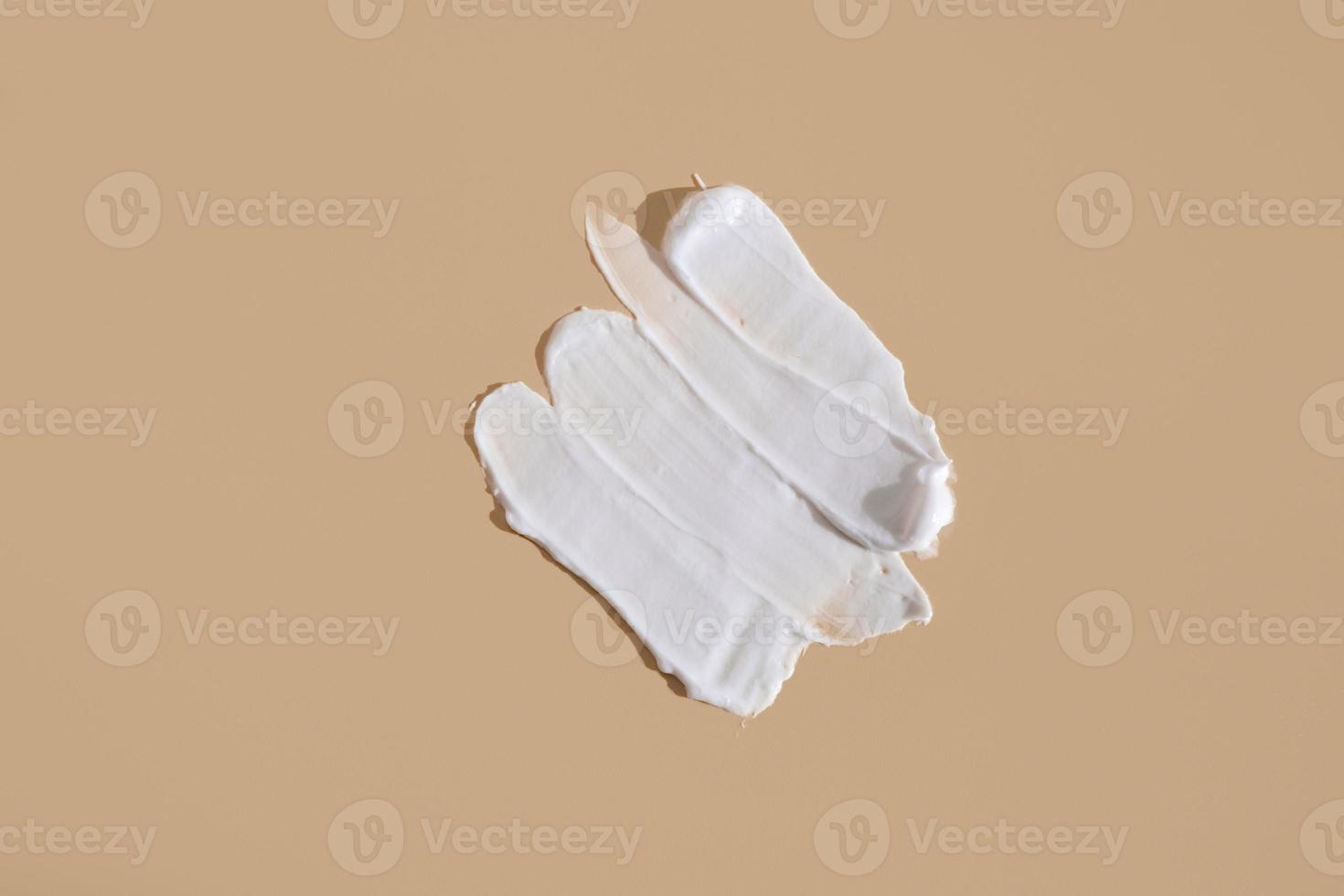 White smear of cosmetic cream on a beige background. Creamy foundation texture isolated. Smear of face cream. Close up of cream texture photo