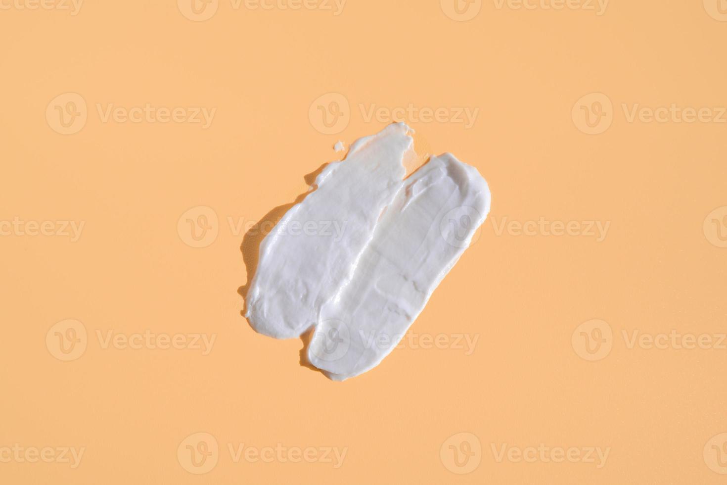 White smear of cosmetic cream on a beige background. Creamy foundation texture isolated. Smear of face cream. Close up of cream texture photo