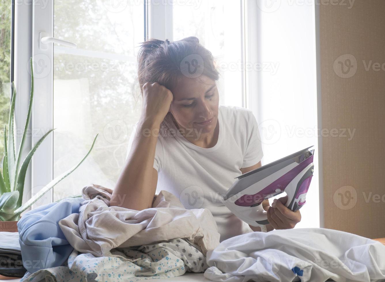 Disappointed unhappy housewife leaning on a pile of laundry on the ironing board photo