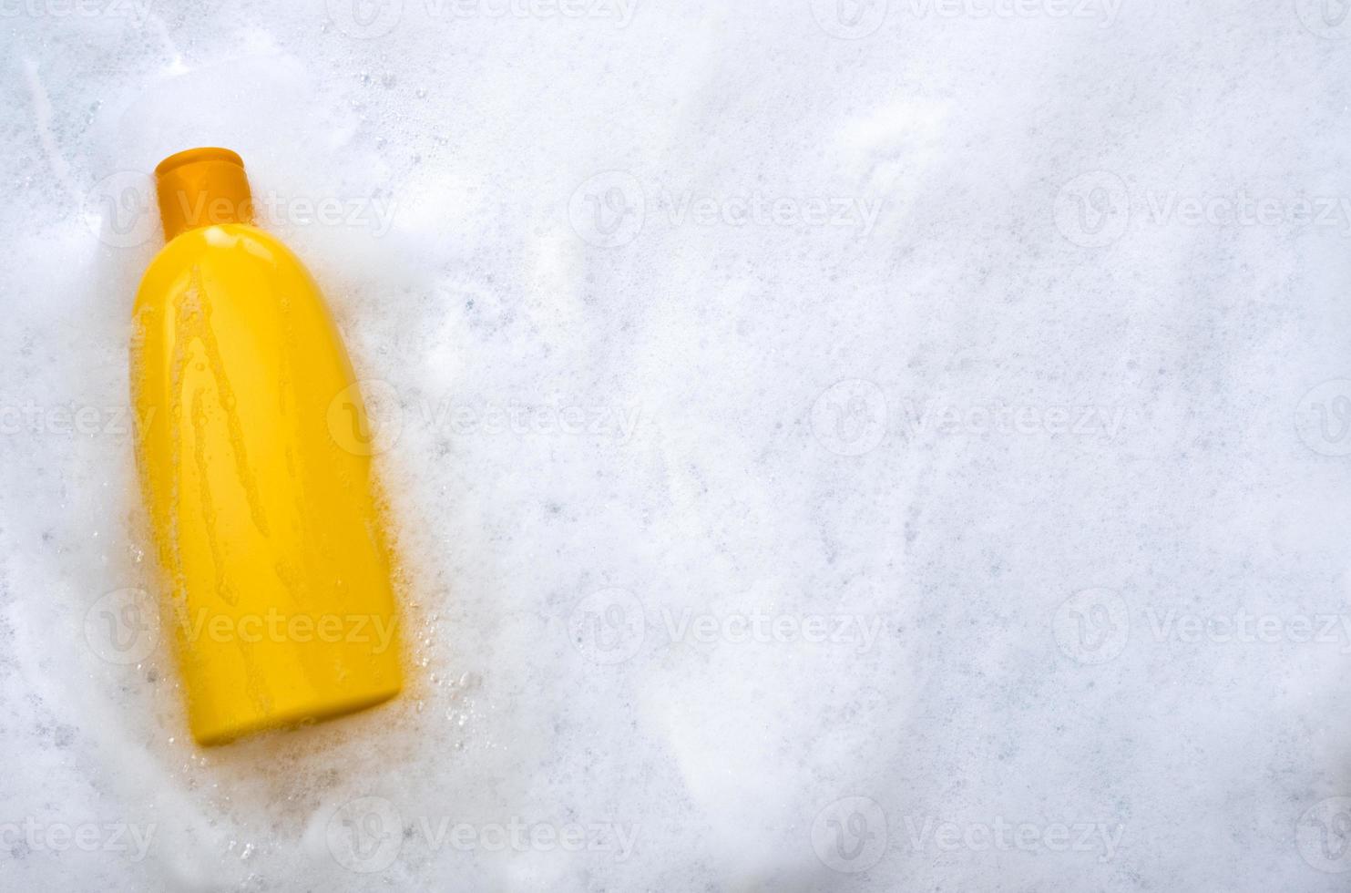 Mockup of a yellow plastic tube with moisturizer, shower gel, shampoo or facial cleanser and gentle soap suds with bubbles on a white background, top view. photo