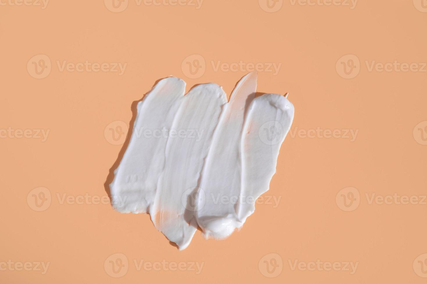 White smear of cosmetic cream on a beige background. Creamy foundation texture isolated. Smear of face cream. Close up of cream texture photo