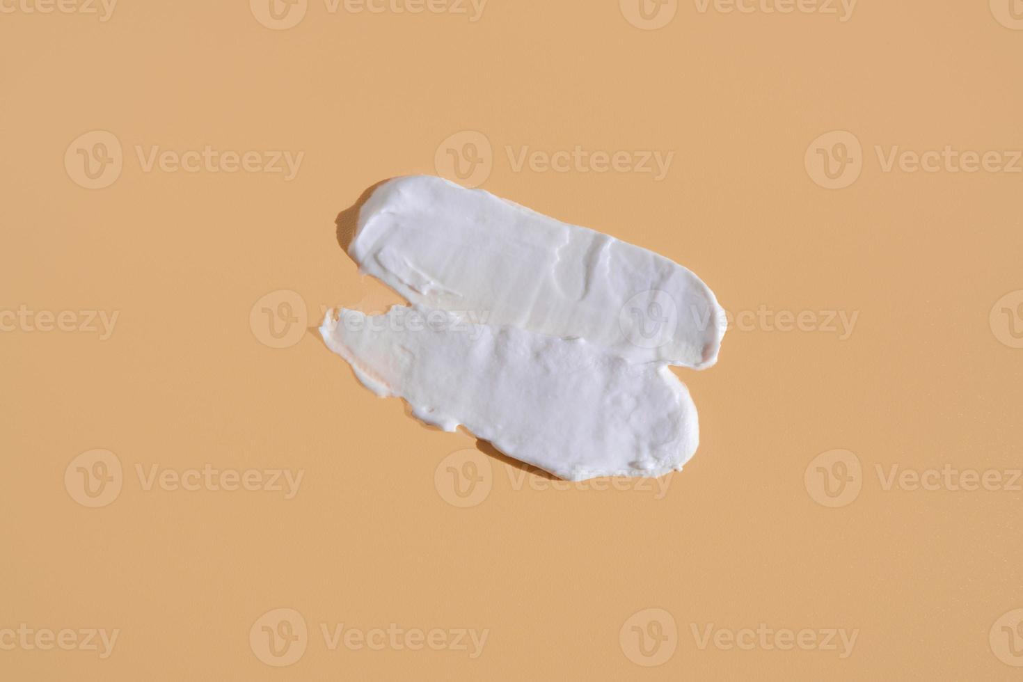 White smear of cosmetic cream on a beige background. Creamy foundation texture isolated. Smear of face cream. Close up of cream texture photo