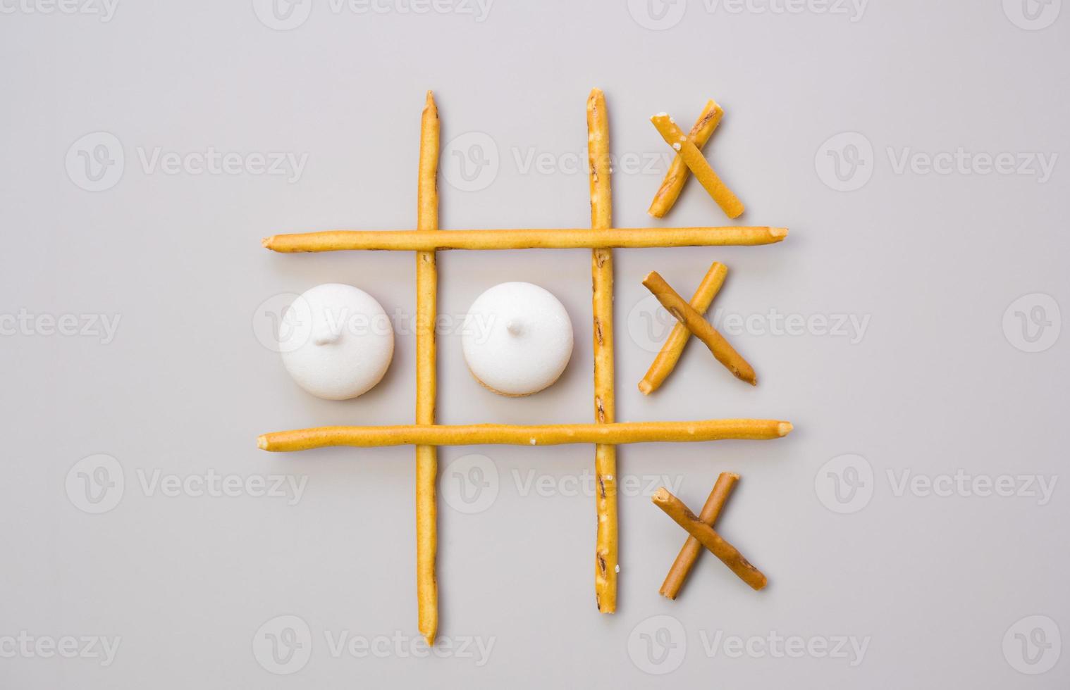 tic-tac-toe from crackers and sticks on a beige background. Food concept. Edible snacks dry sticks with salt and cookies on a white plate. Straws, sticks for crackers. photo