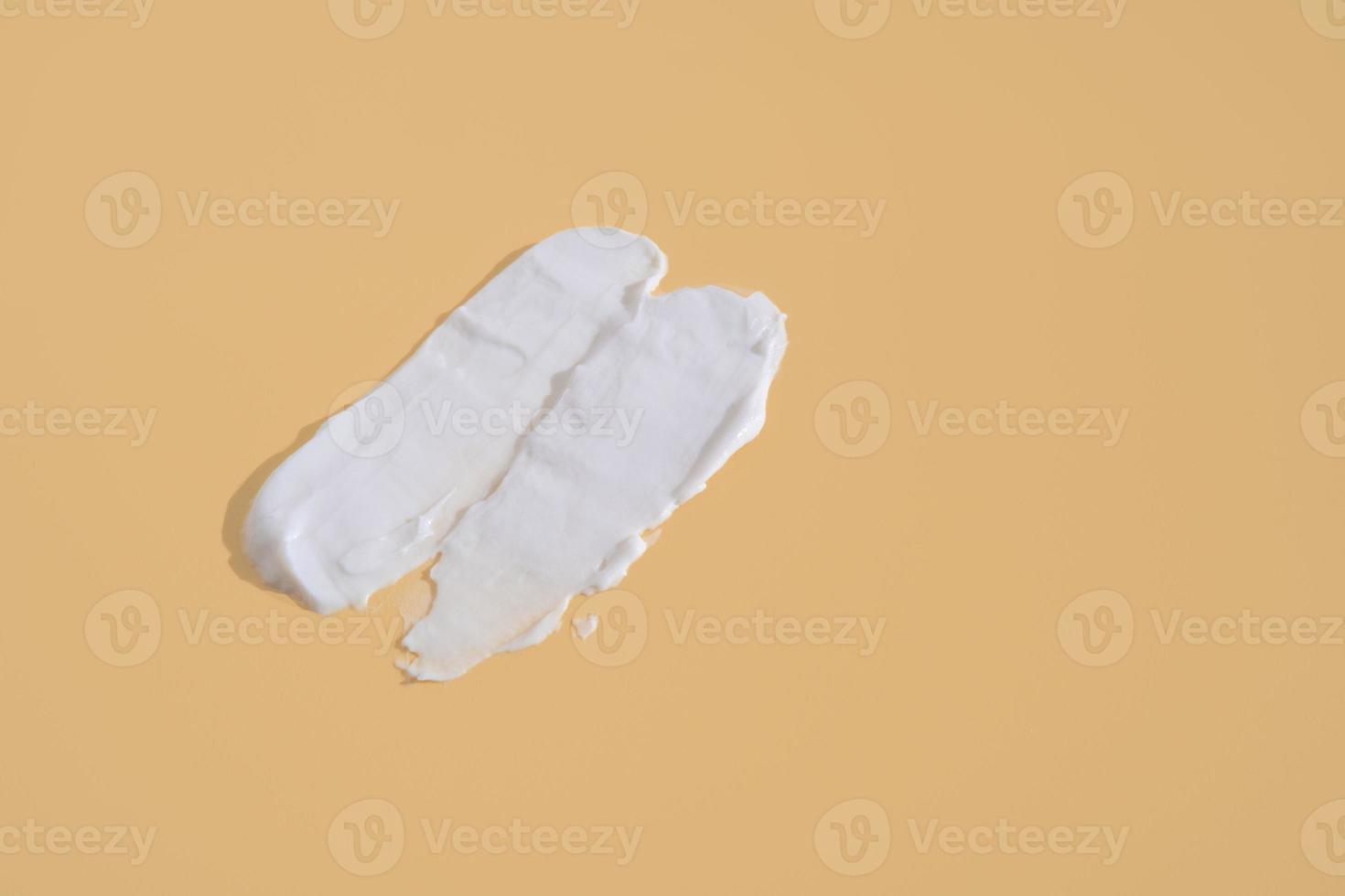 White smear of cosmetic cream on a beige background. Creamy foundation texture isolated. Smear of face cream. Close up of cream texture photo
