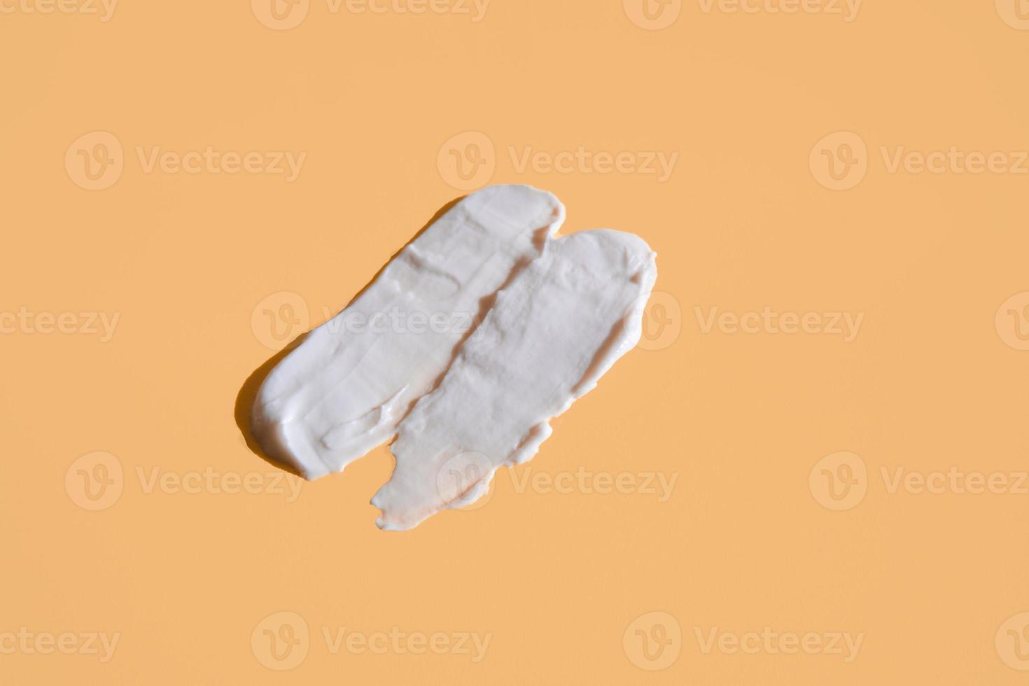 White smear of cosmetic cream on a beige background. Creamy foundation texture isolated. Smear of face cream. Close up of cream texture photo