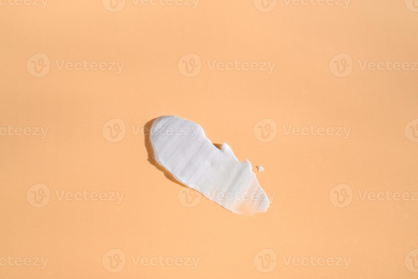 White smear of cosmetic cream on a beige background. Creamy foundation texture isolated. Smear of face cream. Close up of cream texture photo
