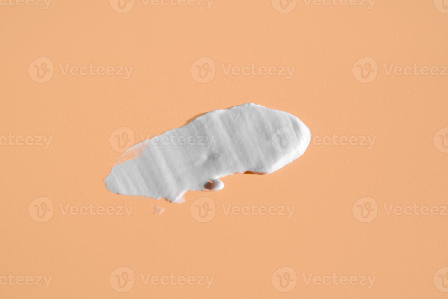White smear of cosmetic cream on a beige background. Creamy foundation texture isolated. Smear of face cream. Close up of cream texture photo