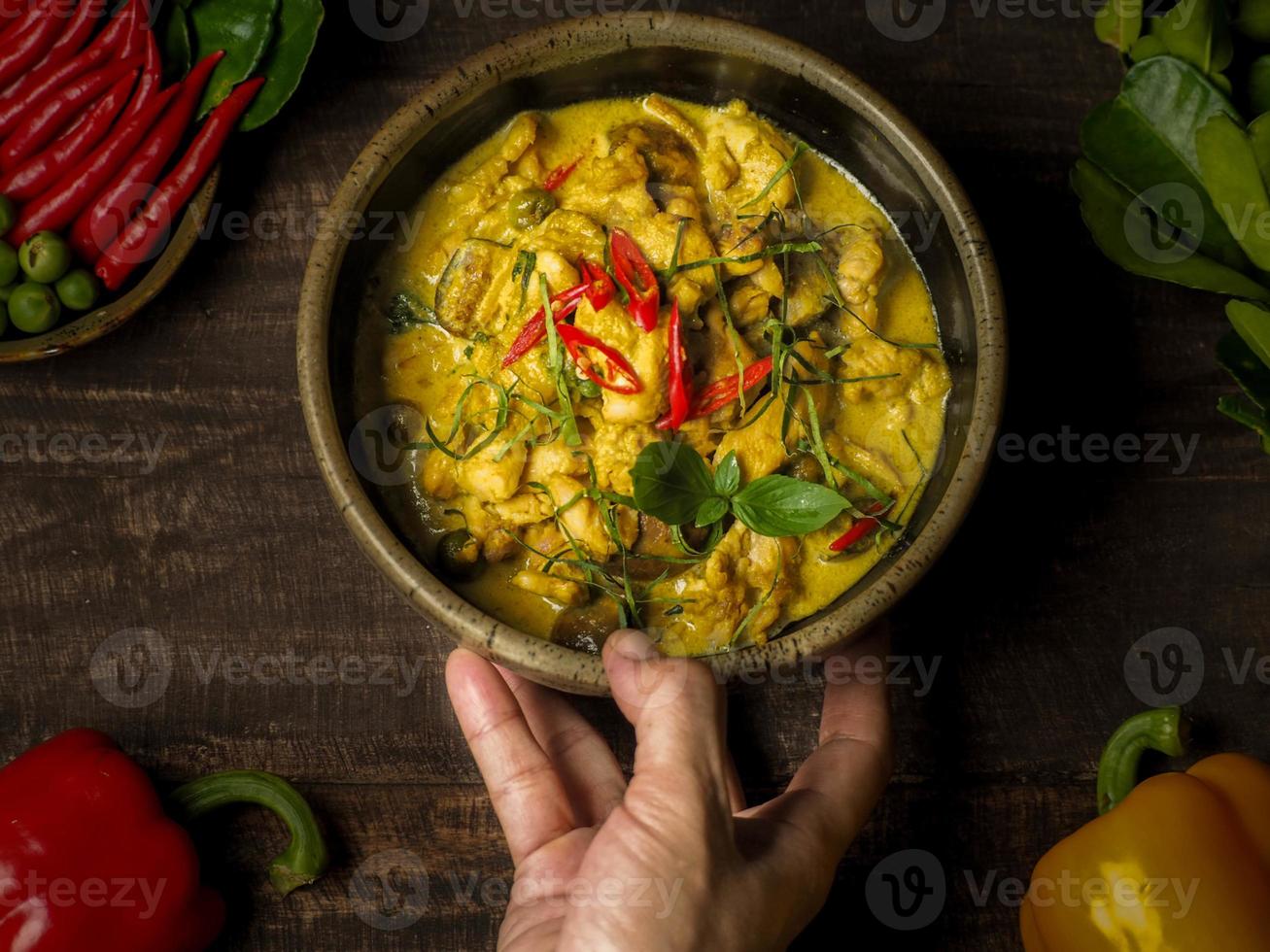A right women hand serve a beautiful chicken green curry on a wood table with a beautiful light photo