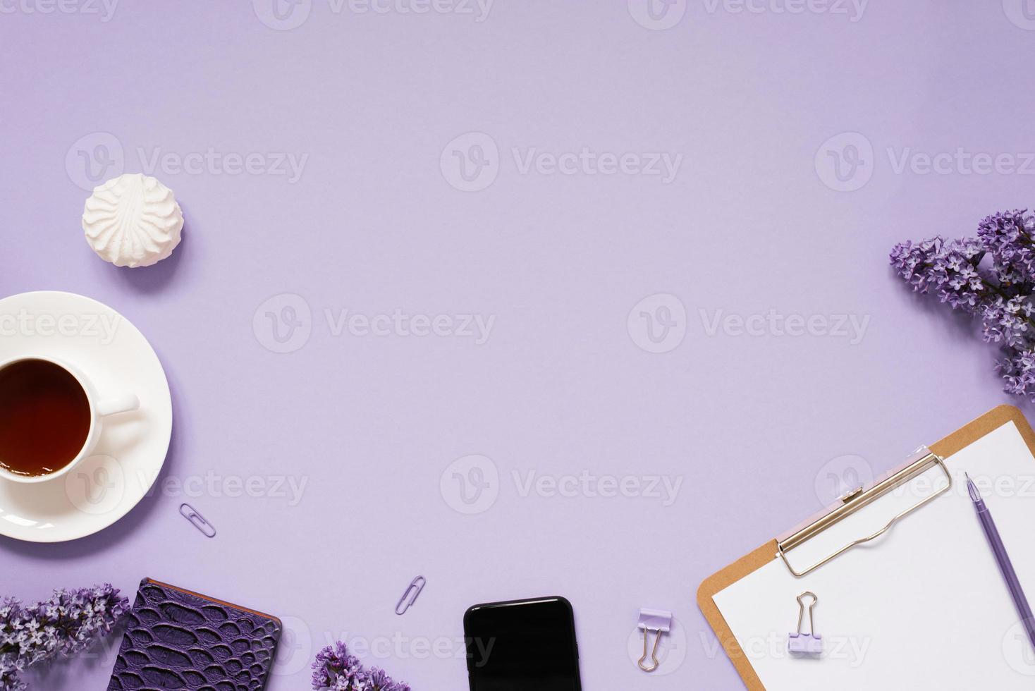 notepad and pen, paper clips and clips with a layout of the place to copy. Home office desktop with top view, decorated with lilac flowers, a cup of tea photo