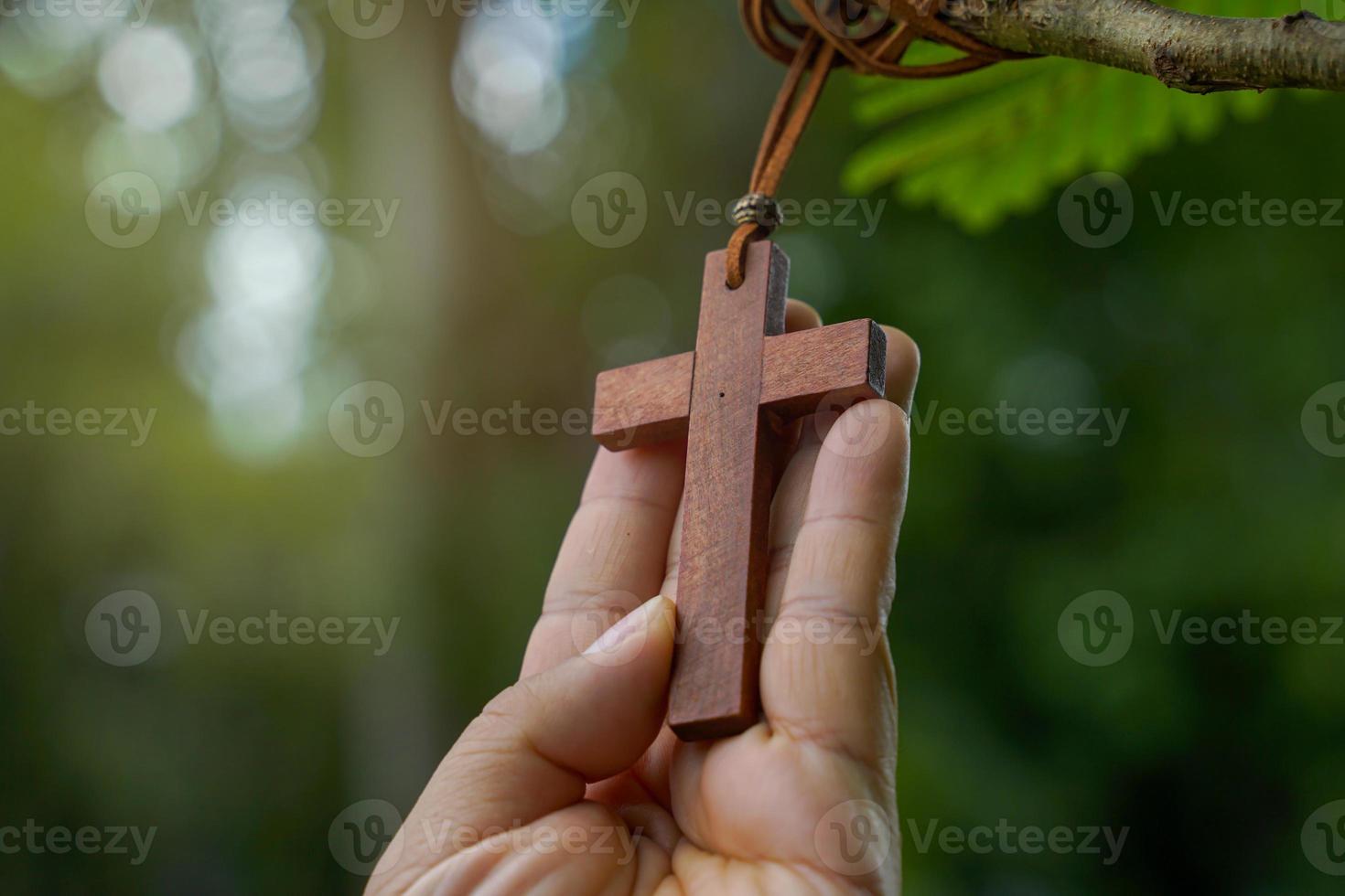 cruz de madera sosteniendo en las manos, concepto de esperanza, amor, perdón y creencia en jesús en todo el mundo. enfoque suave y selectivo, fondo de árbol de bokeh natural. foto