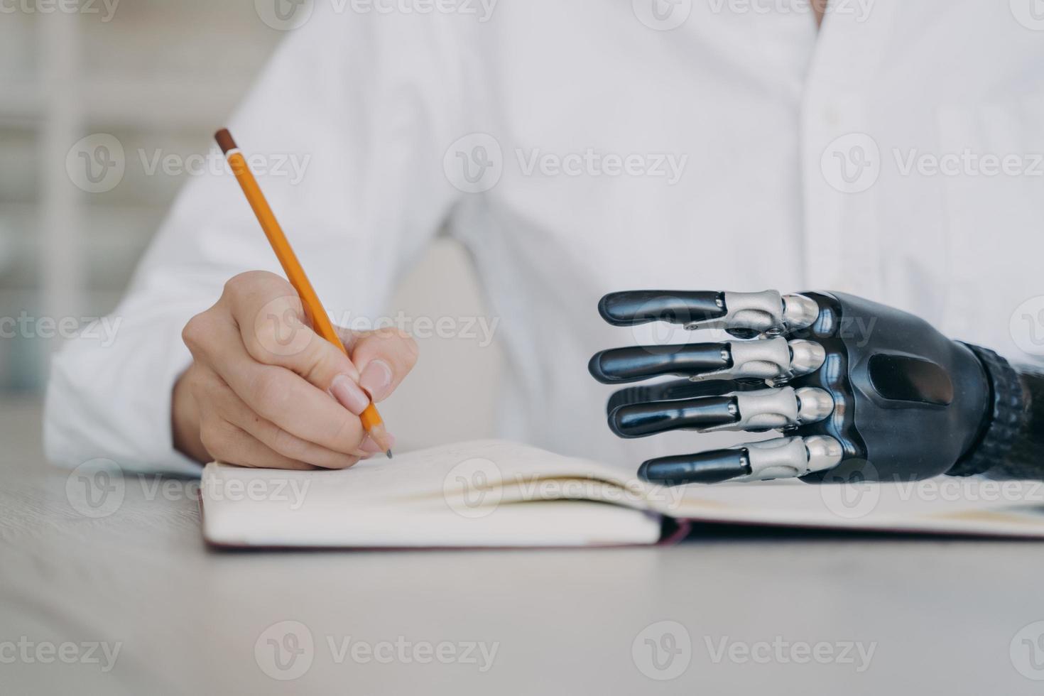 escritura femenina discapacitada con lápiz en el cuaderno, usando un brazo protésico biónico, primer plano. tecnología médica foto