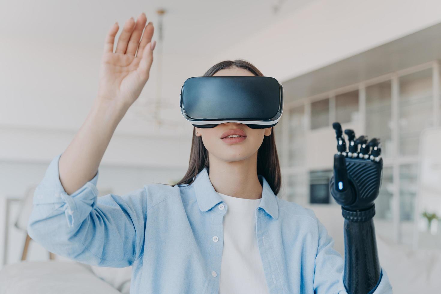 Disabled girl in virtual reality glasses touching air by bionic prosthetic arm. Medical high tech photo